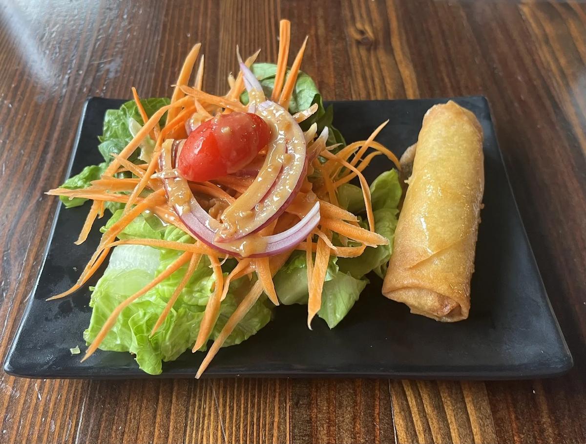 A salad with a crispy spring roll on a black plate